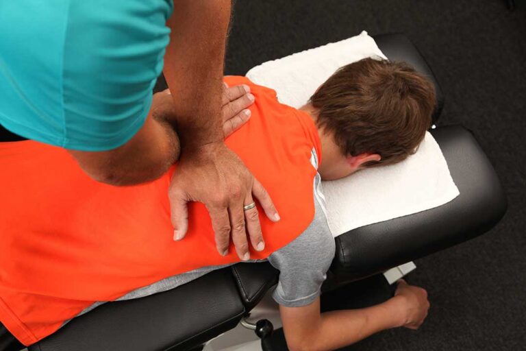 A chiropractor gently assessing a young person's back curvature in a bright, comfortable clinic room.