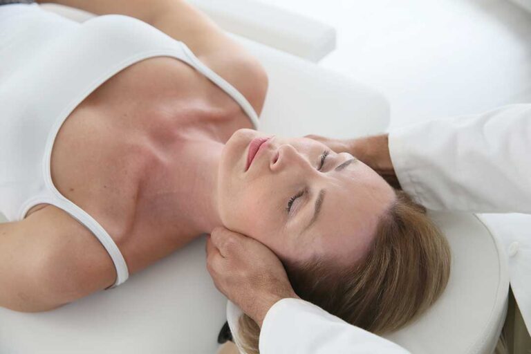 Person stretching beside a bed in a bright bedroom, with one knee raised and shoulders relaxed.